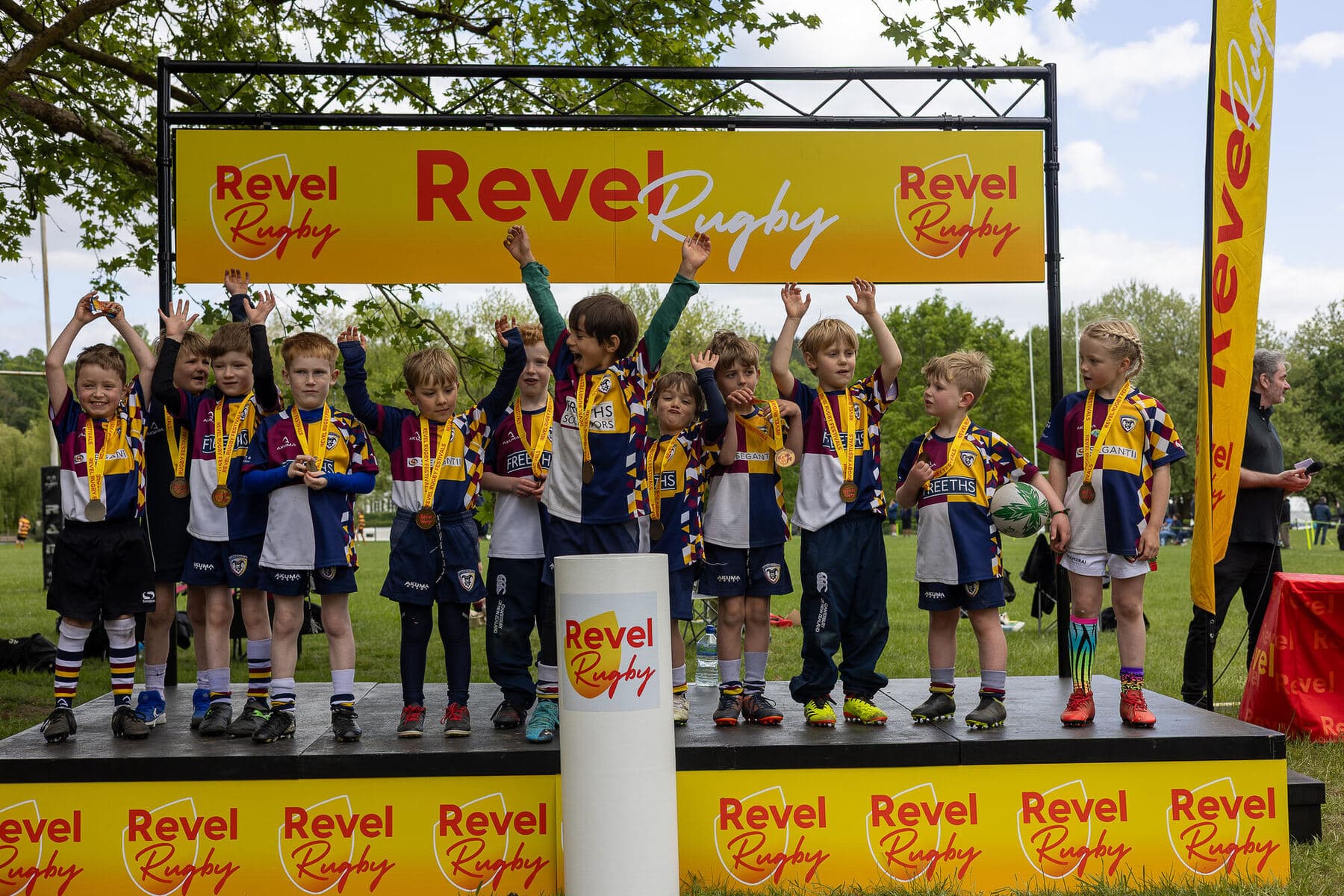 A whole junior team on the Revel Rugby stage with medals round their necks and arms in the air