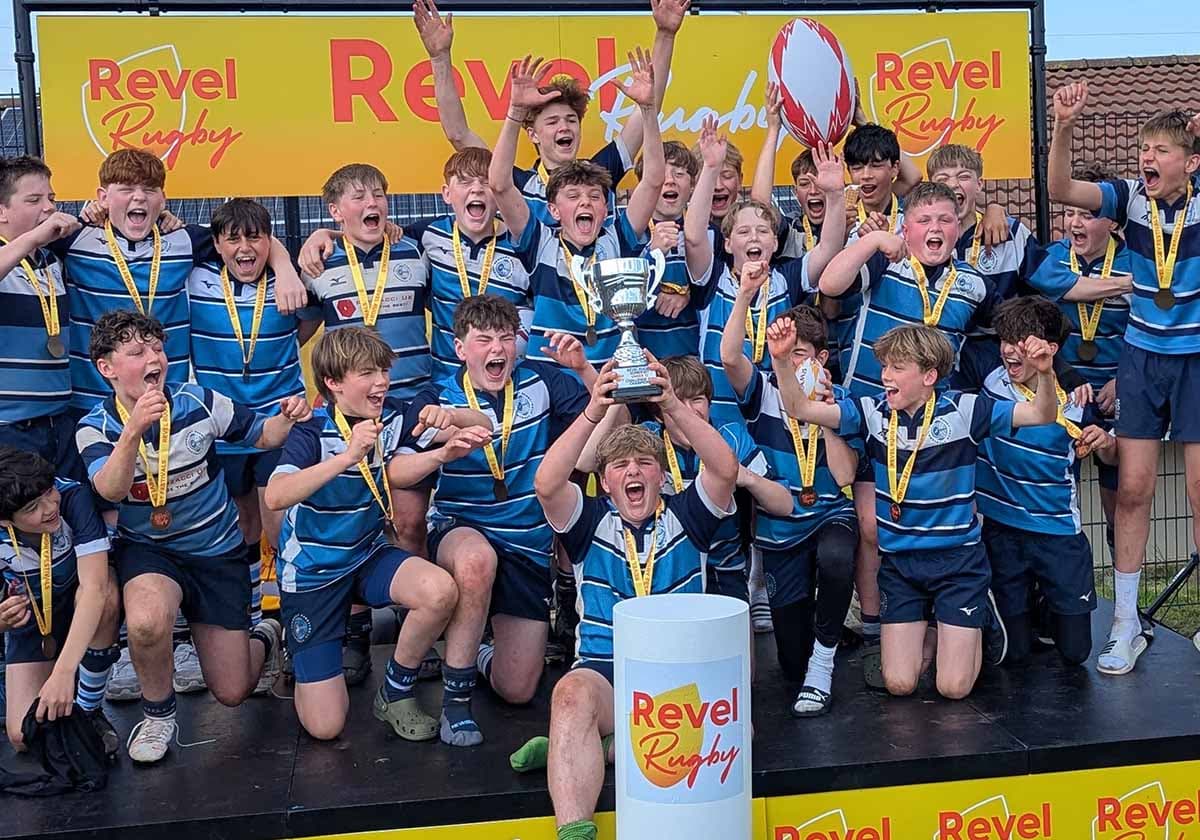 A teenage squad in blue hoops on the podium with medals, a trophy held high and arms raised