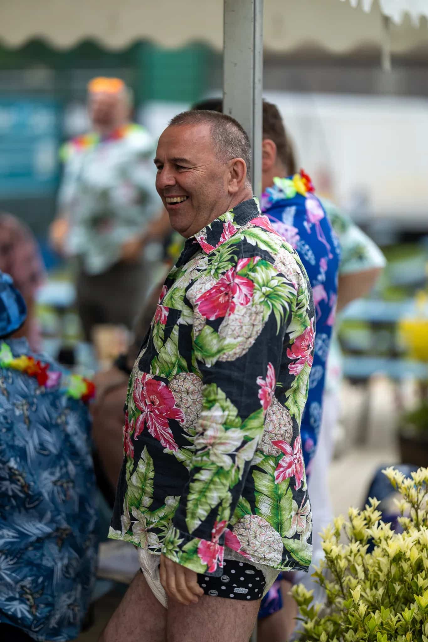 A grinning man in a Hawaiian shirt enjoying the atmosphere at a rugby festival